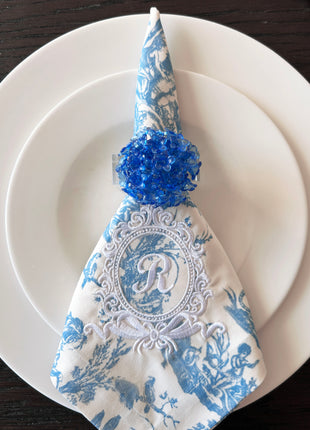 Decorative table setting with a blue acrylic blossom napkin ring on toile de jouy patterned napkin