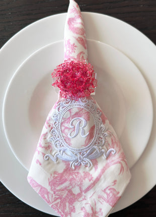 Decorative table setting with a pink acrylic blossom napkin ring on toile de jouy patterned napkin