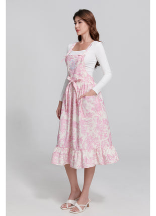 Model wearing a pink toile de jouy floral apron with pretty ruffle hemline on a gray background