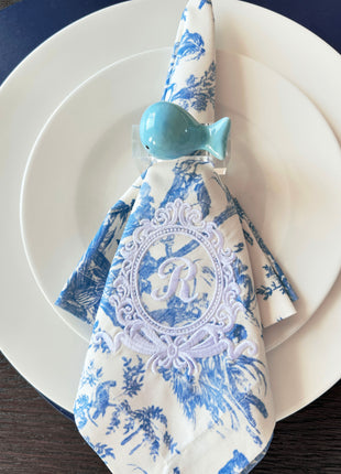 Decorative table setting with a blue ceramic whale napkin ring on toile de jouy patterned napkin
