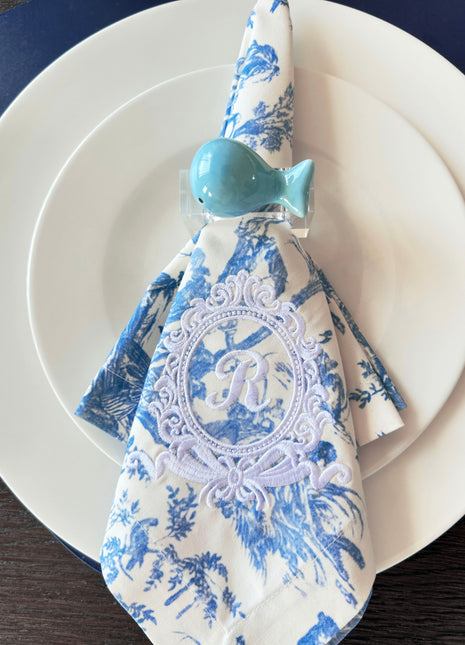 Decorative table setting with a blue ceramic whale napkin ring on toile de jouy patterned napkin